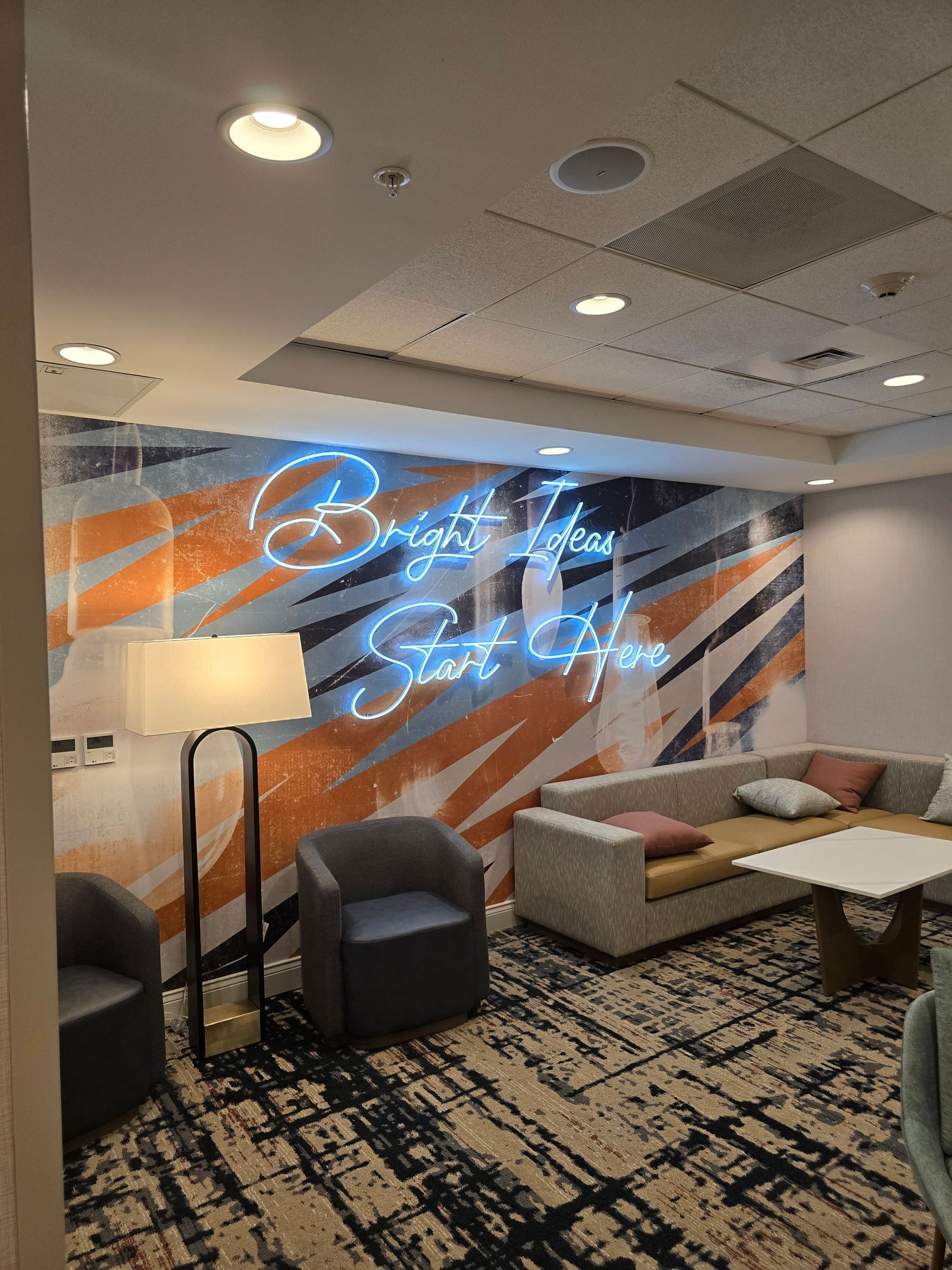 Modern lounge with neon wall art, orange and blue accents, sofas, and a patterned rug.
