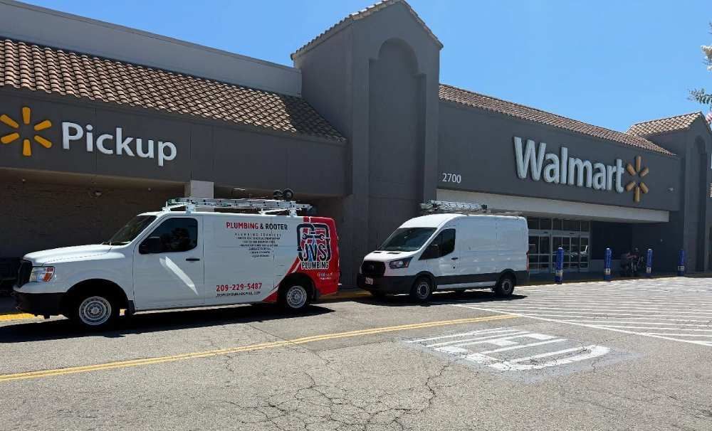 Two delivery vans parked outside a Walmart pickup area on a sunny day