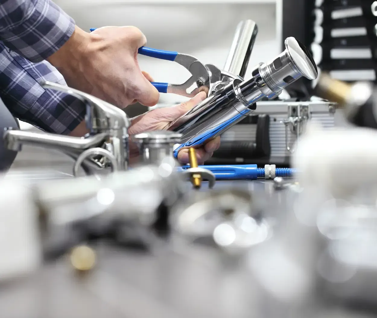 Hands using a wrench to tighten chrome pipes in a mechanical workshop, with blurred tools in foreground