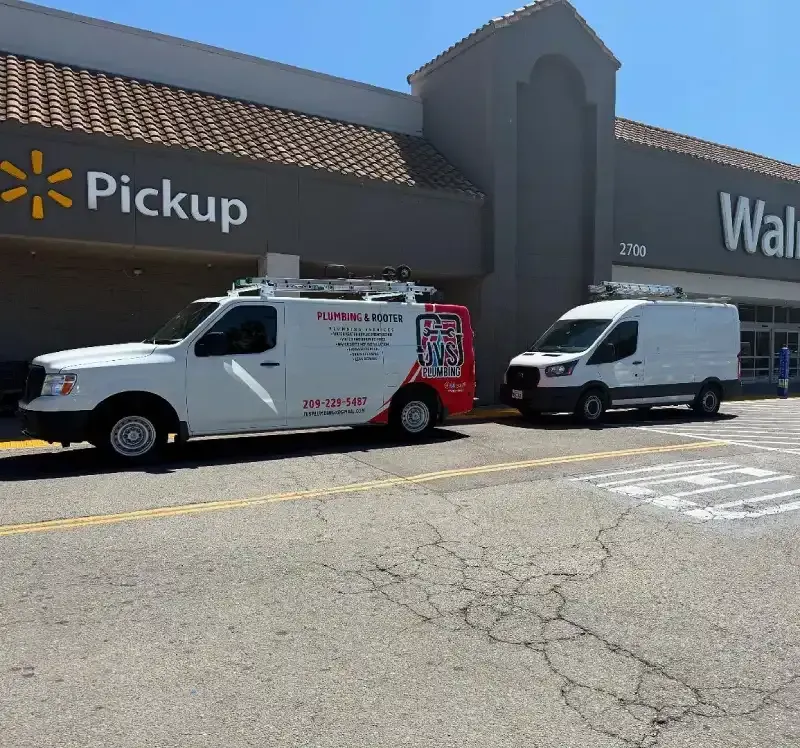 Two white service vans parked outside a Walmart pickup entrance on a sunny day