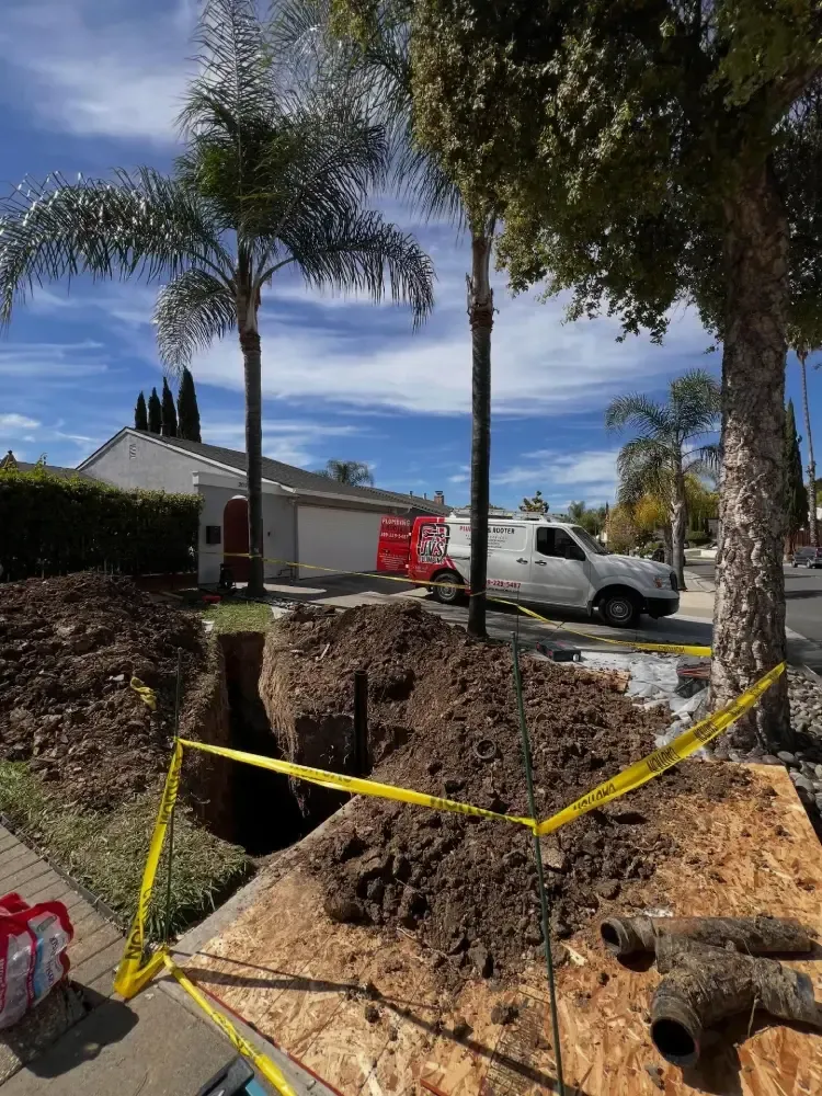 Trenched dirt excavation in a front yard with yellow caution tape, palm trees, and a white pickup truck nearby