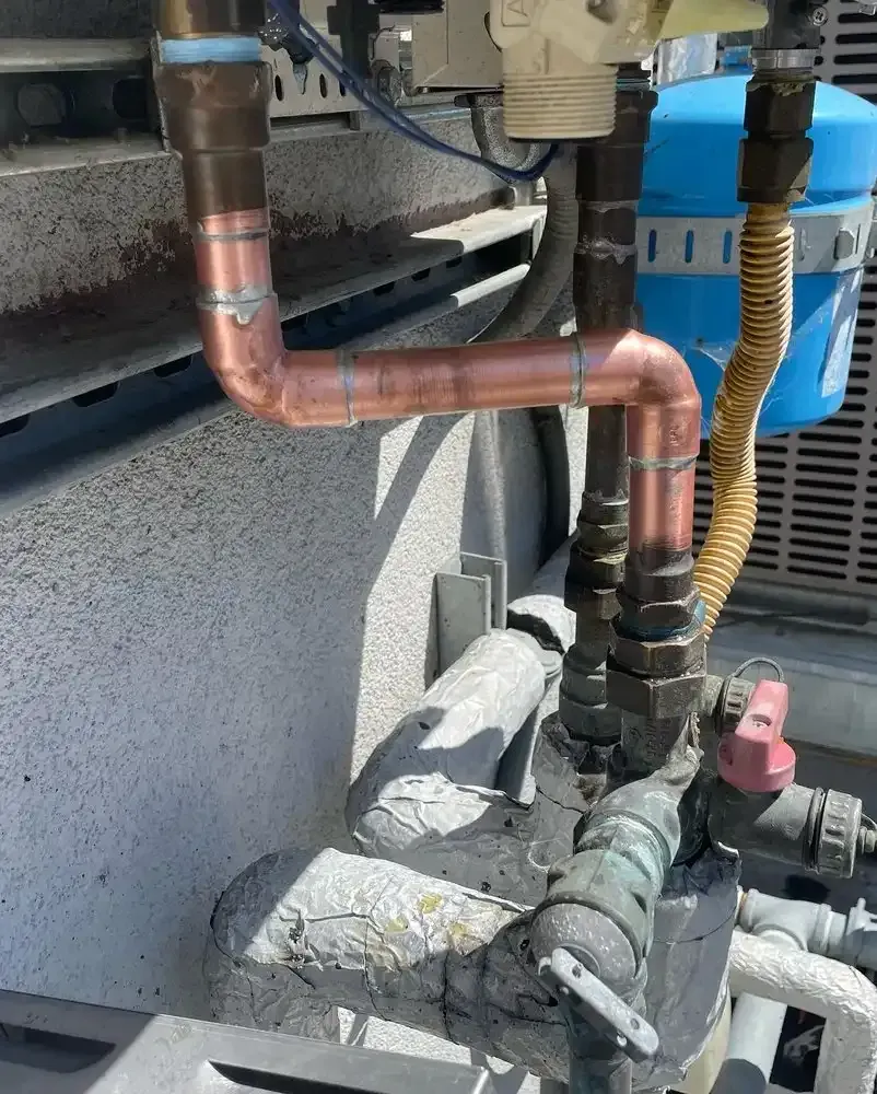 Copper pipes and valves beside a blue industrial unit, showing exterior HVAC plumbing.