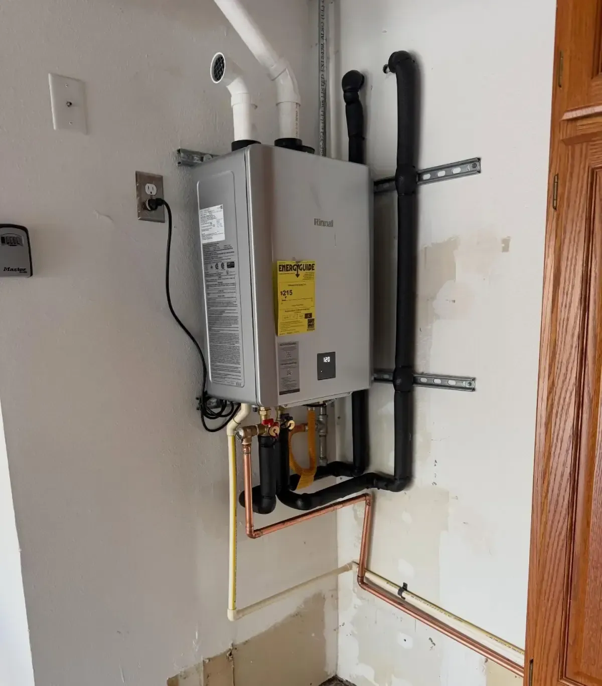 Wall-mounted tankless water heater with exposed copper piping and black vent pipes in a utility closet.
