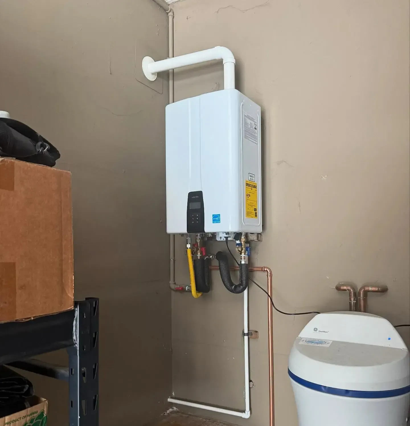 Wall-mounted white water heater with pipes and a white water softener in a beige utility room