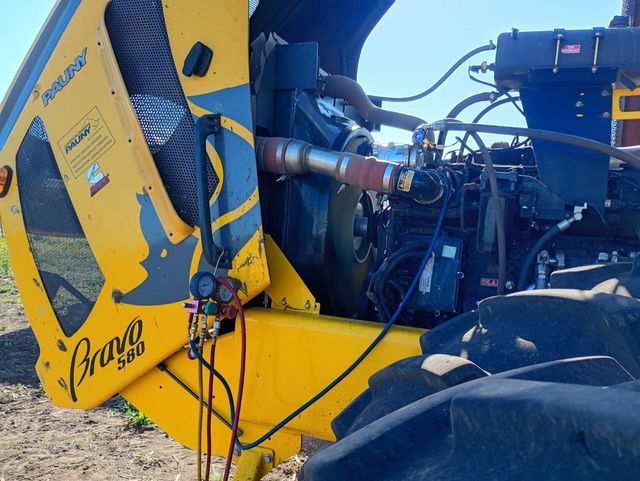 Máquina agrícola amarilla con el motor al descubierto y un gran neumático negro, en primer plano al aire libre