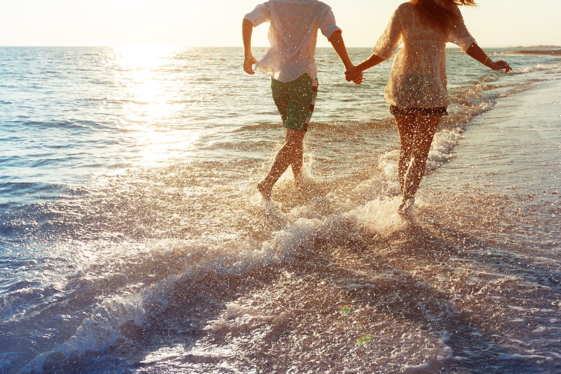 Two people holding hands and running through ocean surf at sunset.