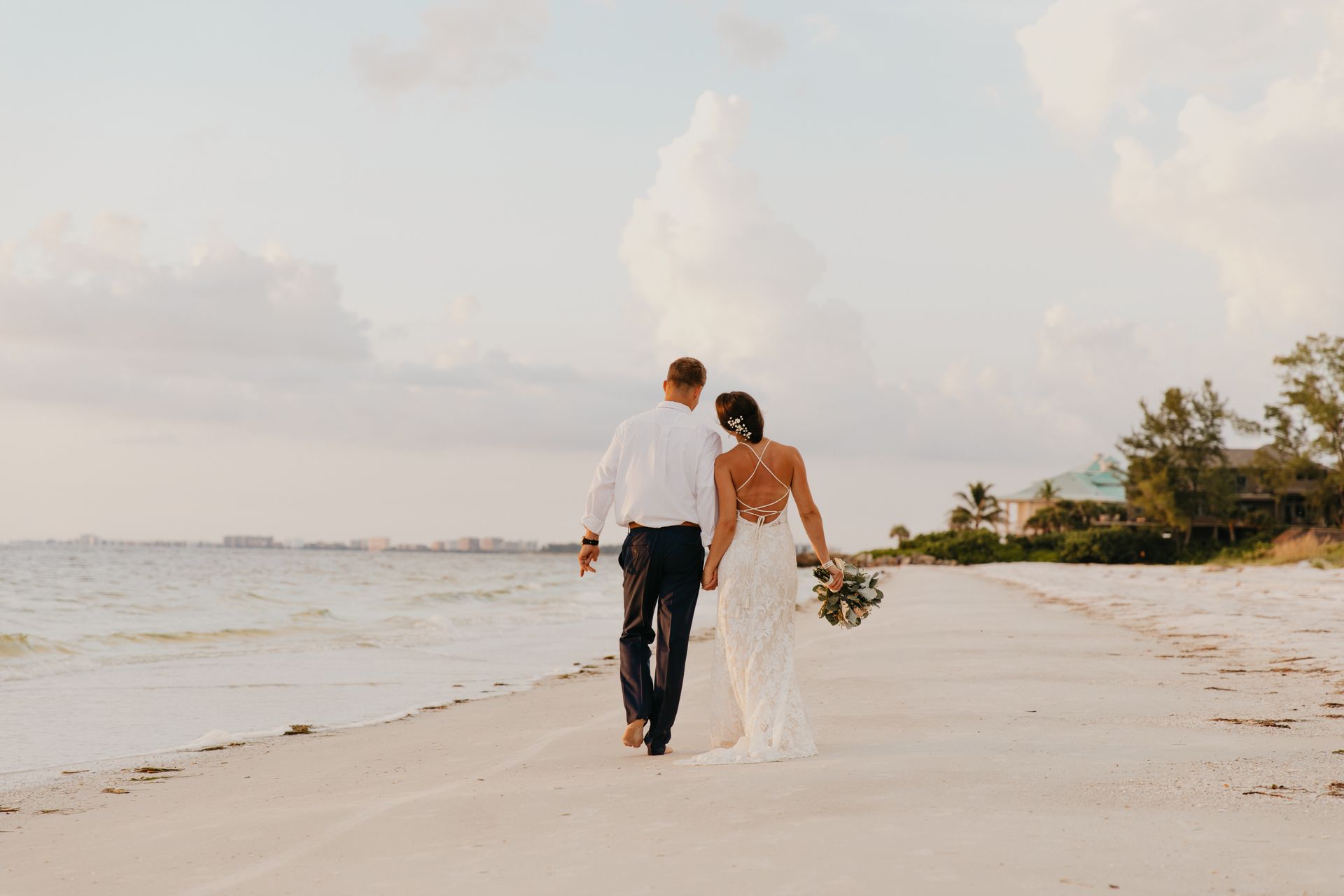 Couple walking hand in hand on a sandy beach at sunset.