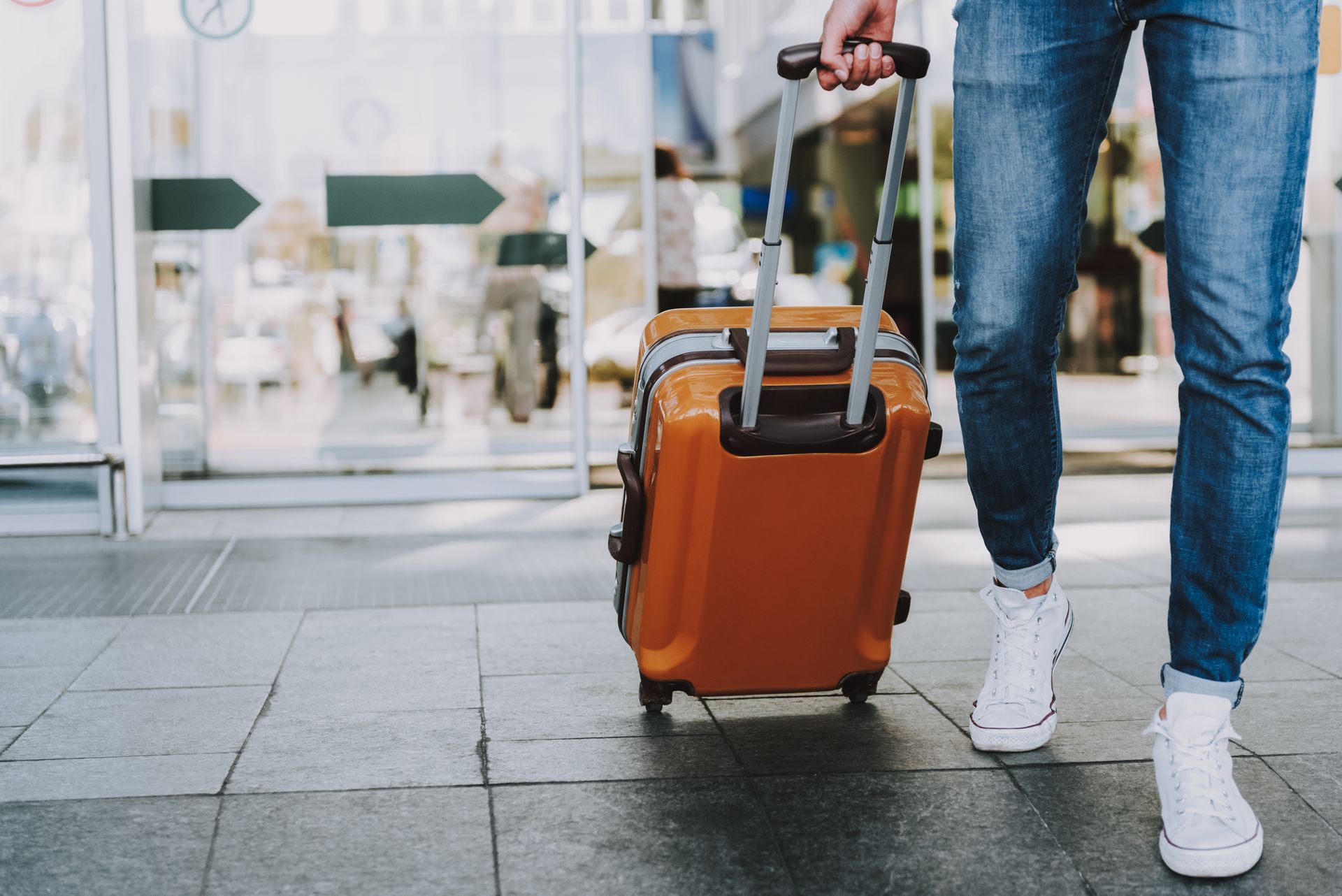 Traveler pulling an orange suitcase past a glass entrance.