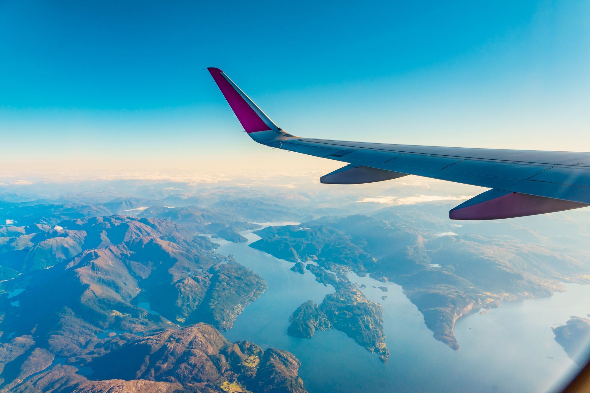 Airplane wing over snowy mountains and a blue lake seen from above.