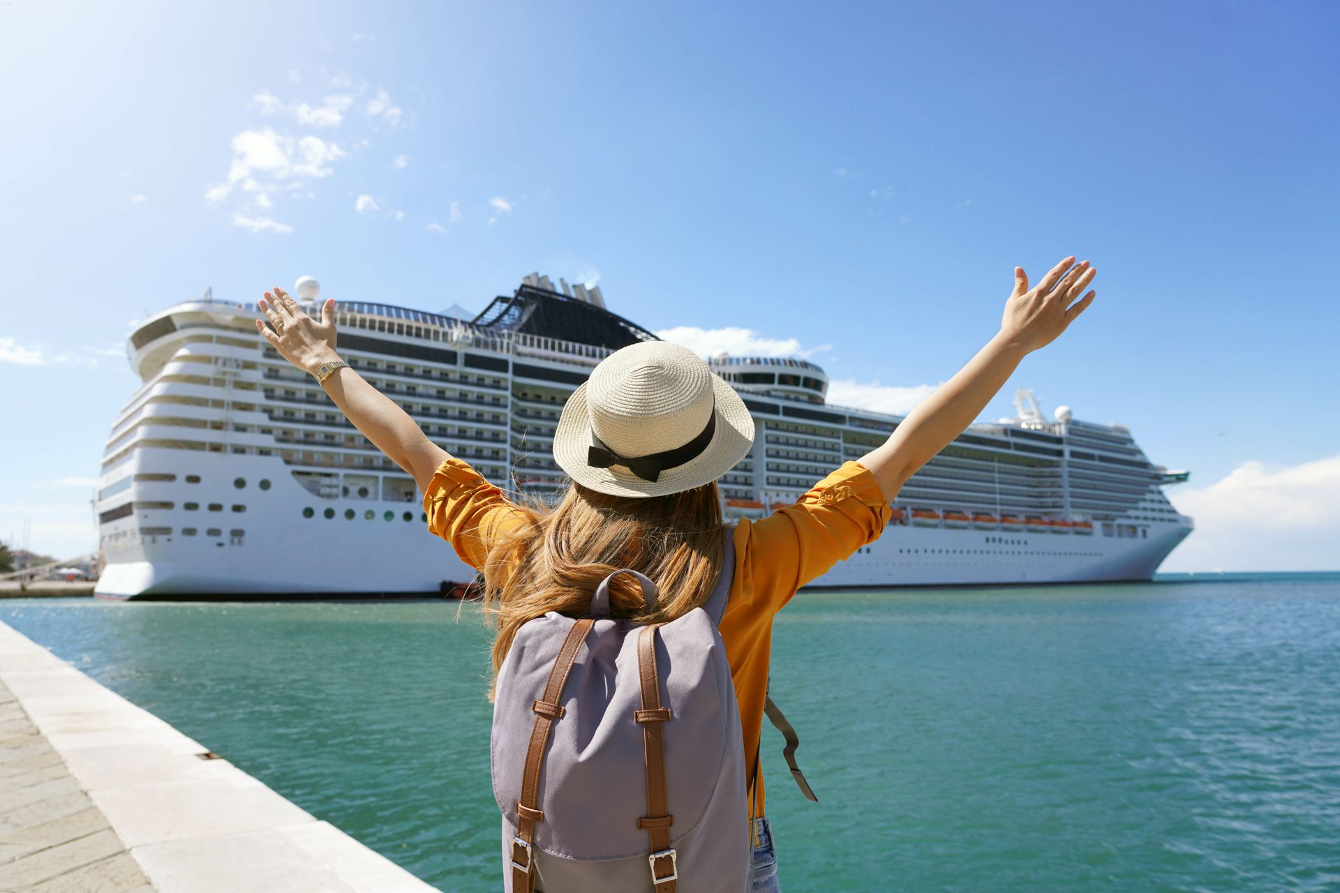 Traveler with arms raised faces two cruise ships in a sunny blue harbor.
