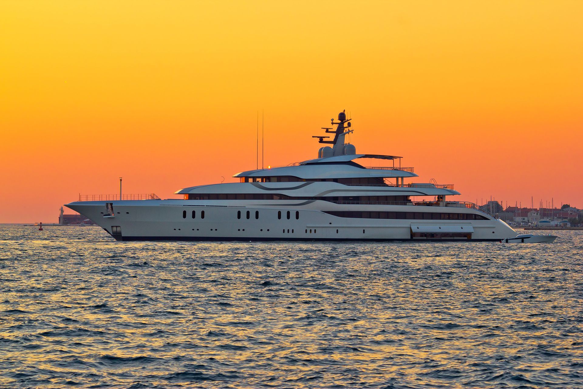 Luxury yacht on calm water at sunset, silhouetted against an orange sky.