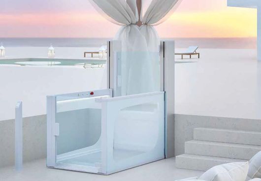 Ascensore esterno bianco con pareti in vetro su una terrazza con vista sulla spiaggia e sul mare.