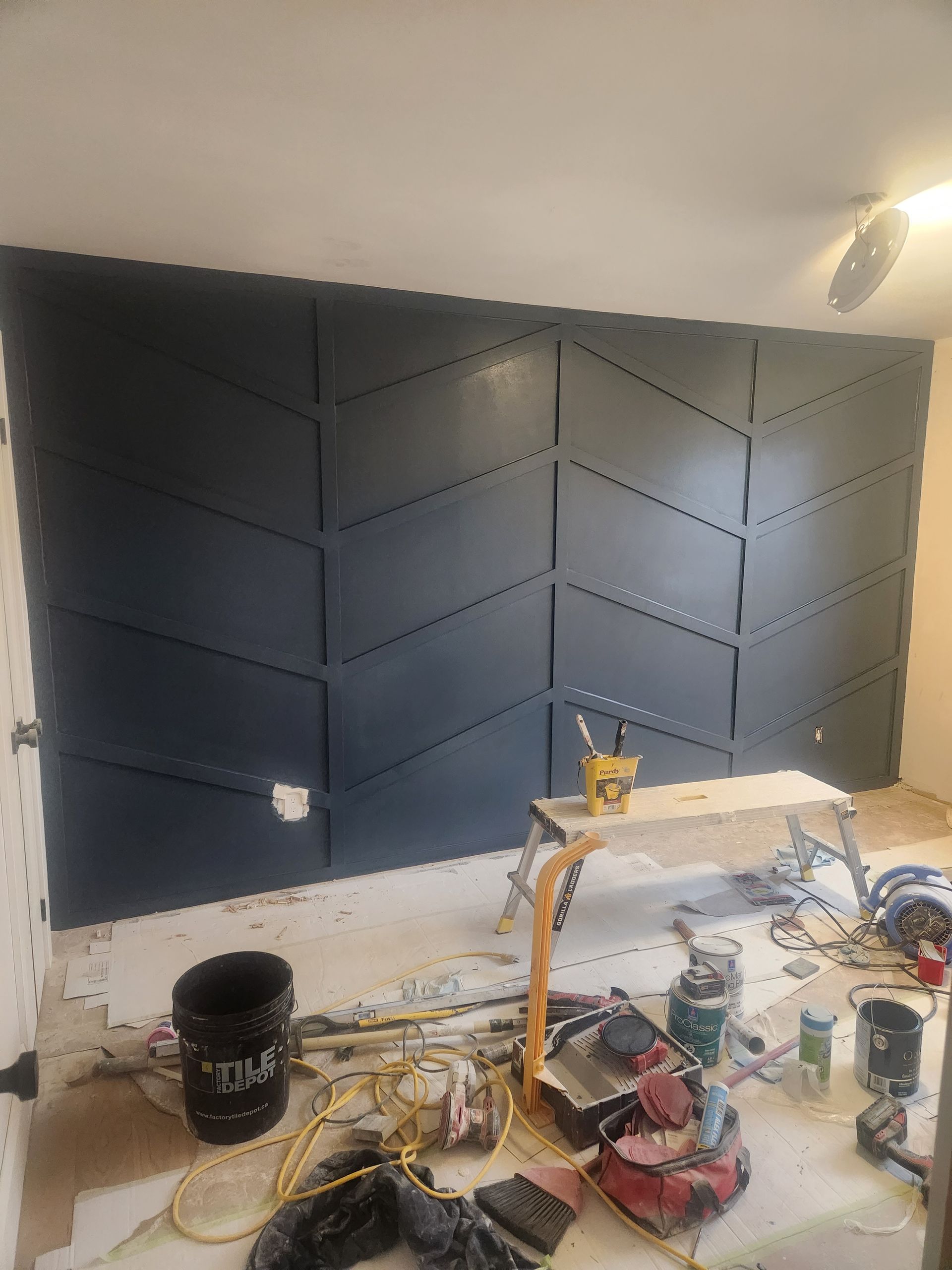 A navy blue geometric accent wall under construction; tools and paint on the floor.