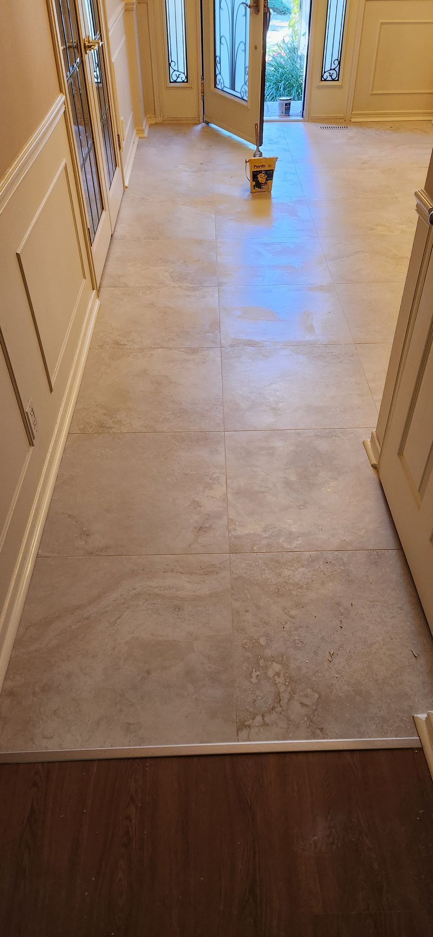 Hallway with new tile floor, leading to front doors, and white paneled walls.