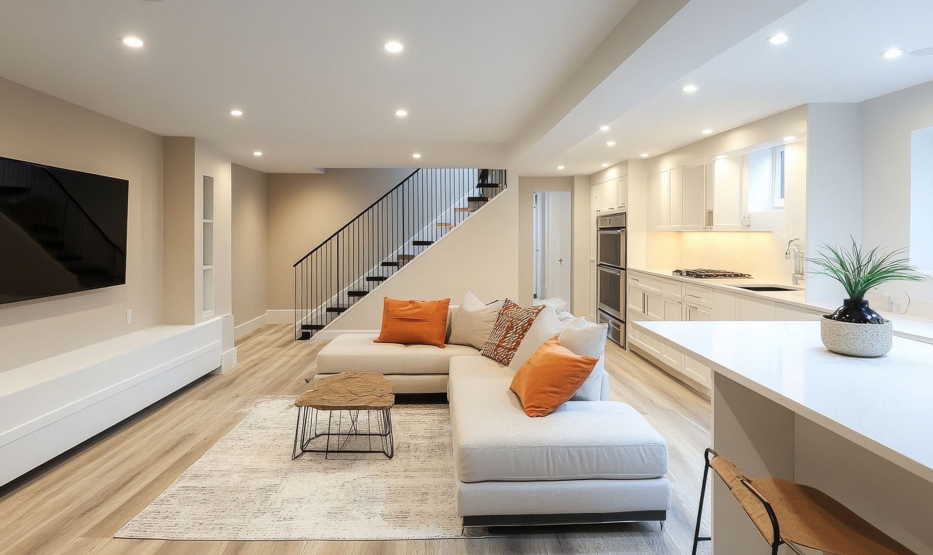 Modern living space: light-colored walls, sectional sofa, kitchen island. Staircase leads upwards.