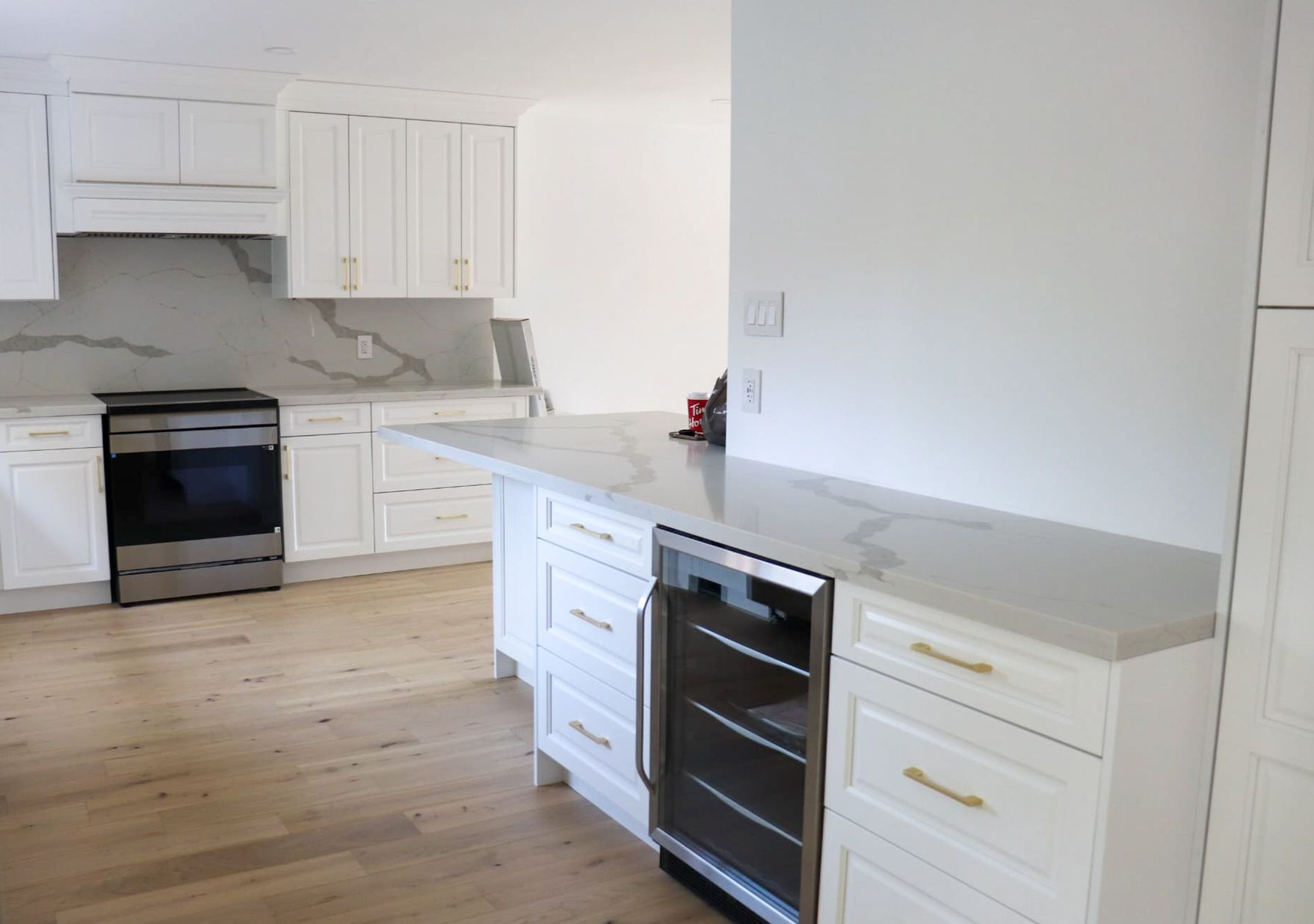 White kitchen with stainless steel appliances, light countertops, and blonde wood floors.