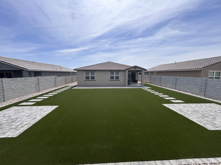 Modern backyard with artificial turf, white stepping stones, and a gray house under a cloudy sky