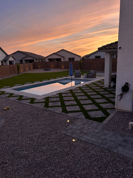 Backyard putting green with artificial turf, white stone border, and a small flag under a clear blue sky