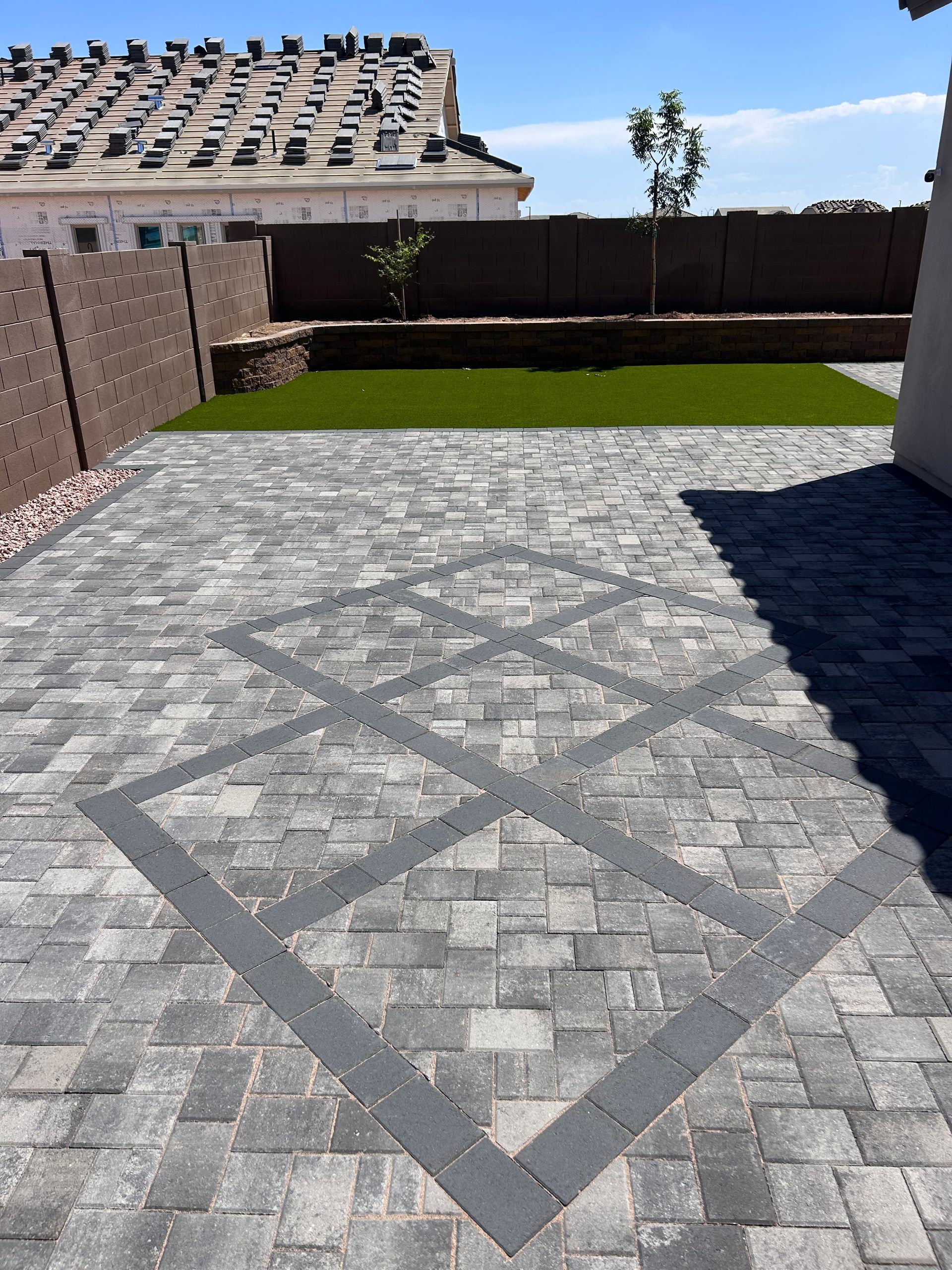 Backyard paver patio with diamond pattern, bordered by brick walls and a small grassy lawn.