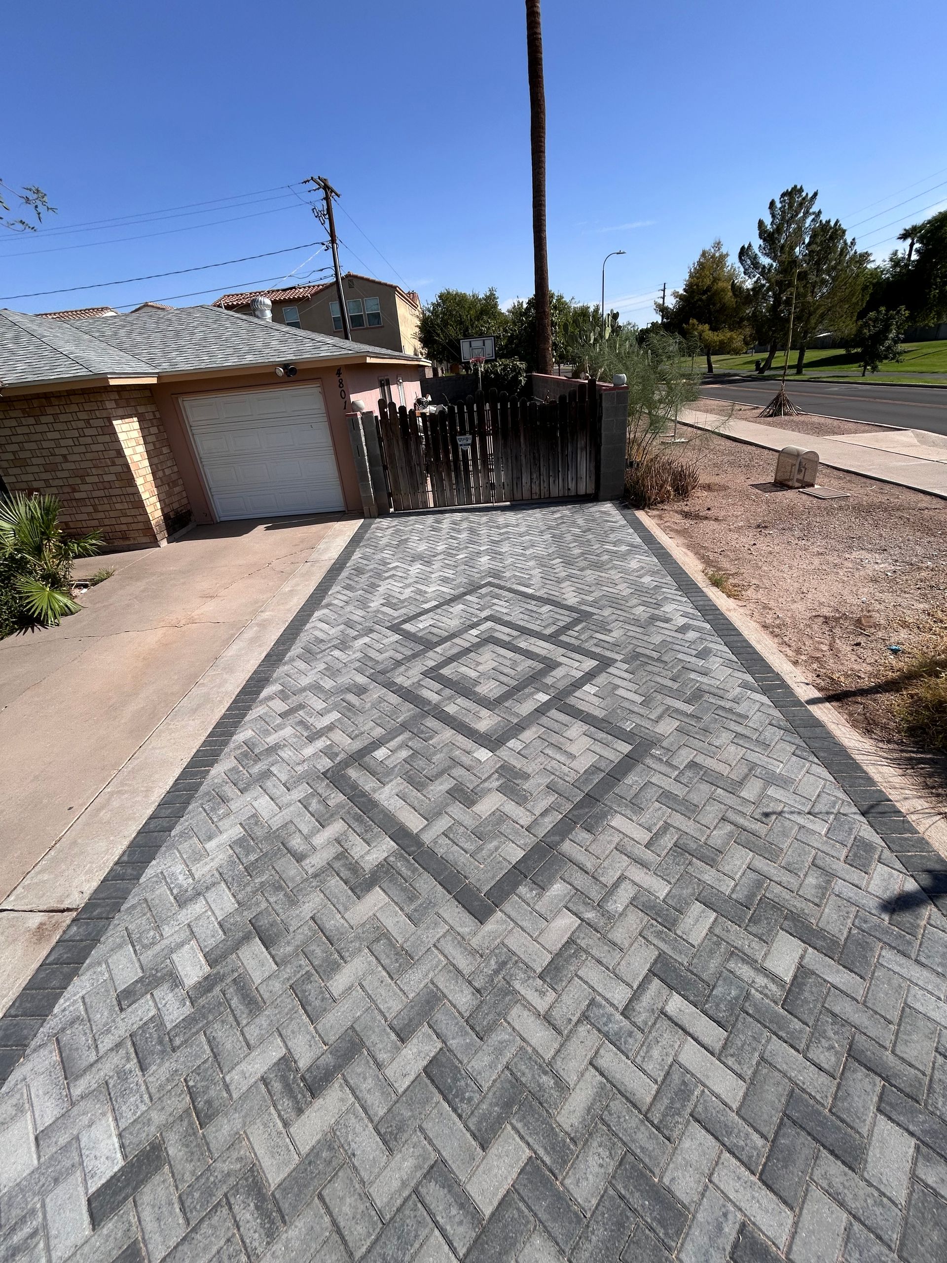 Brick-pattern driveway leading to a garage gate beside a house, with a patterned concrete design in the foreground