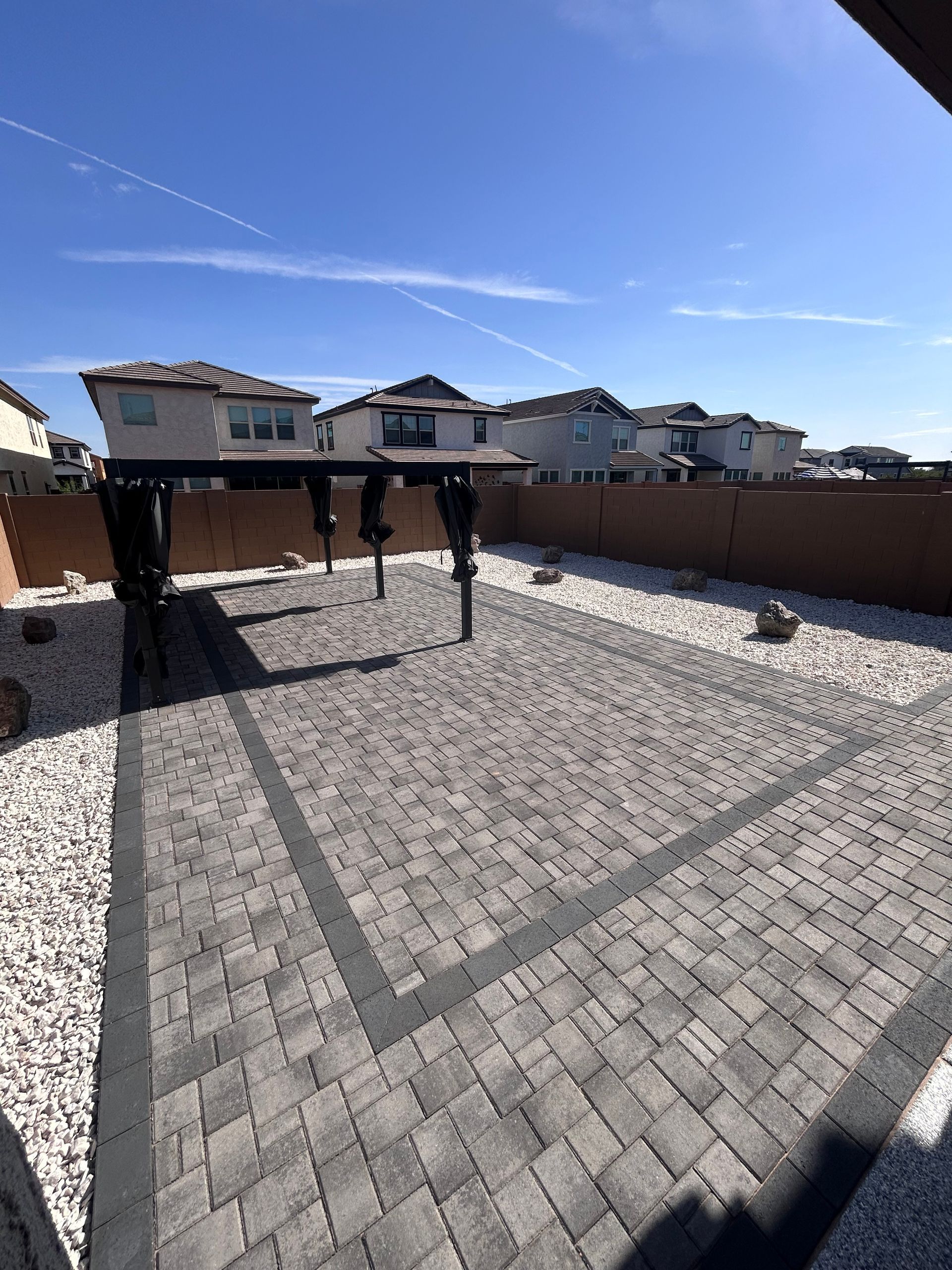 Backyard with gray paver patio, brown fence, and two hanging umbrellas under a clear blue sky