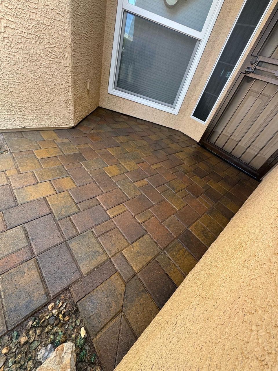 Tiled patio with multi-colored bricks in front of a stucco wall, a window, and a security door.