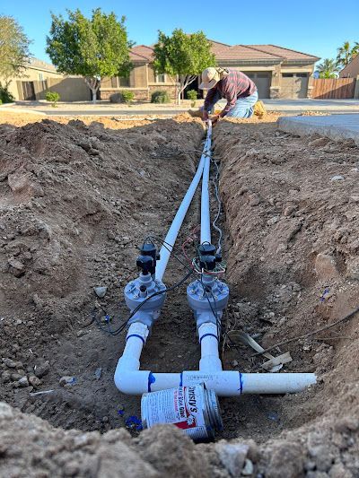 A man is working on a sprinkler system in the dirt.
