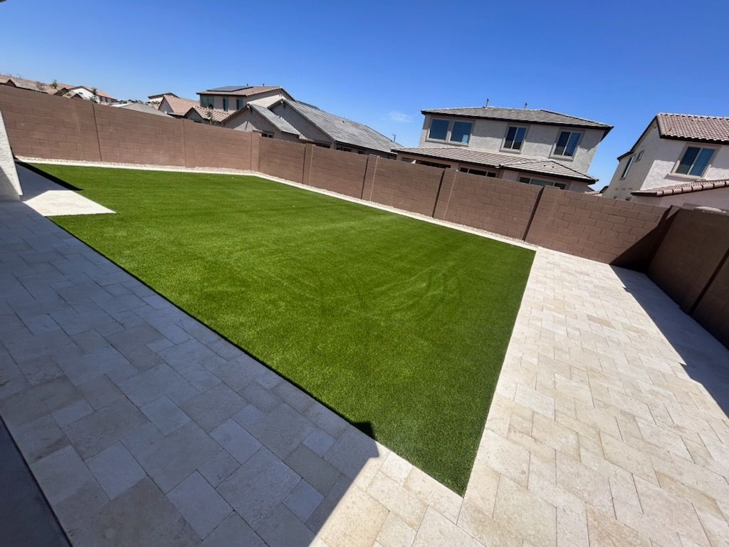 Backyard with green lawn, beige paver patio, and tall privacy walls under a clear blue sky