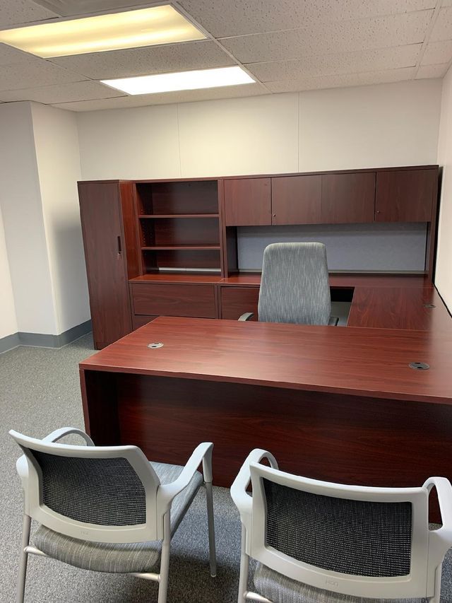 Two chairs are sitting in front of a wooden desk in an office.