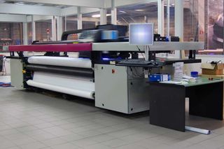 A large printer is sitting in a room next to a desk.