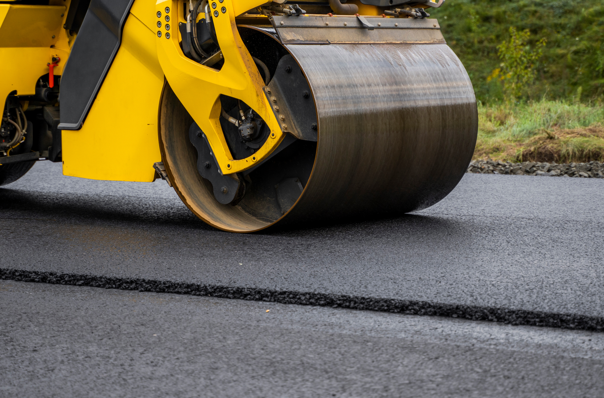 A man is standing next to a machine that is laying asphalt on a road.