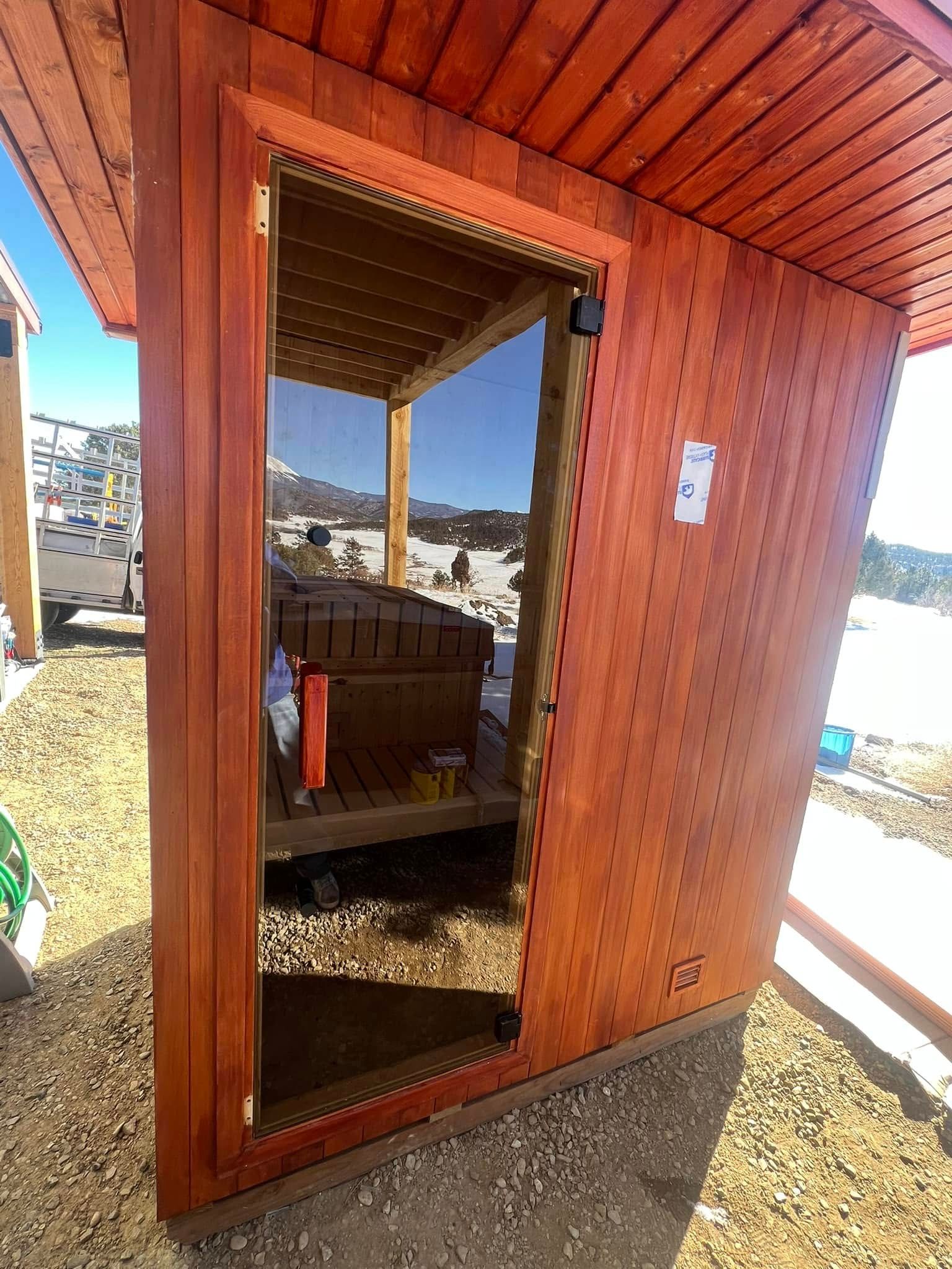 A wooden shed with a glass door is sitting on top of a dirt field.