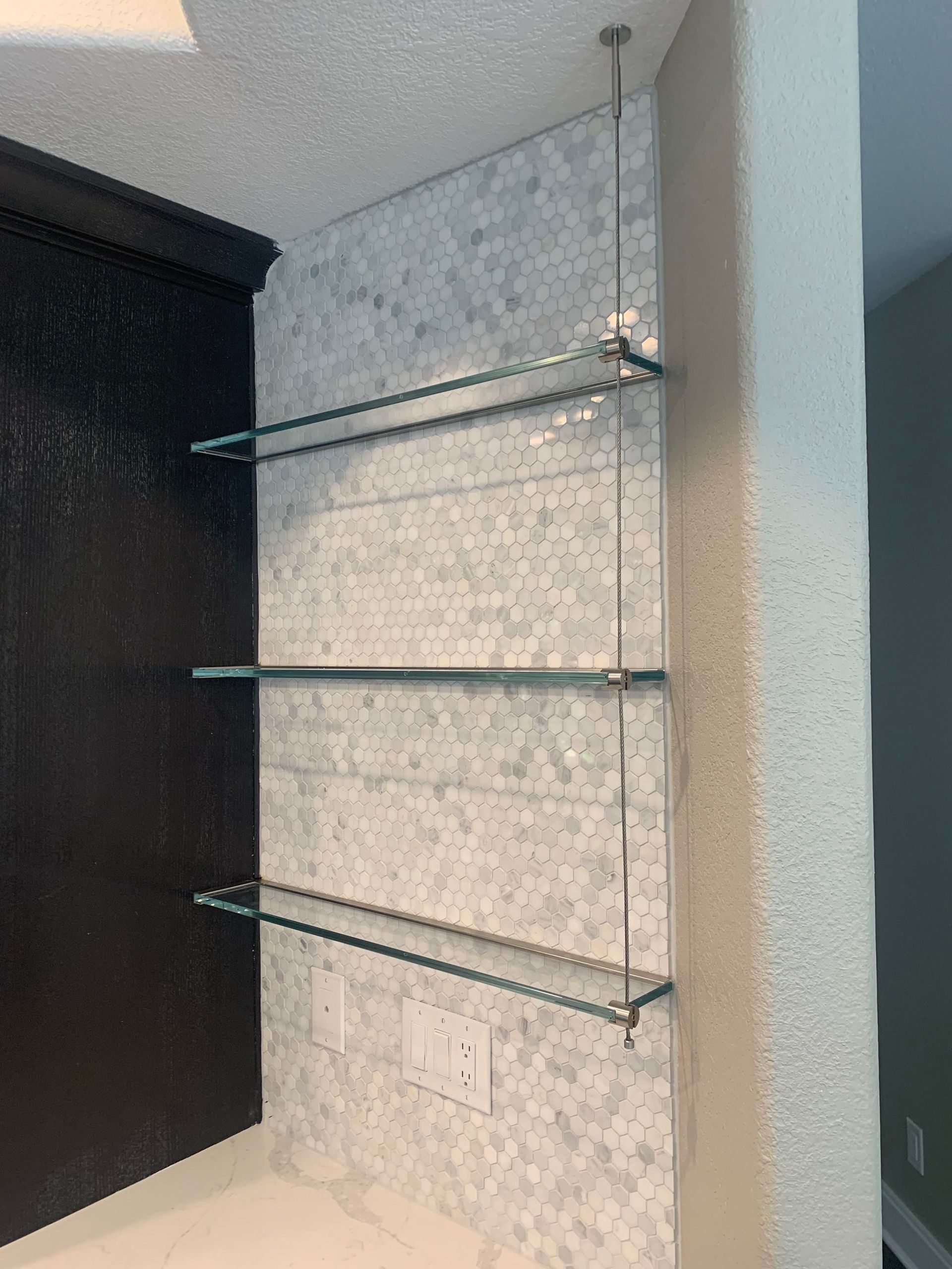 A bathroom with three glass shelves hanging from the ceiling.