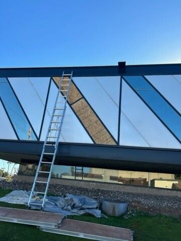 Ladder leaning on a modern glass wall during construction, with tarps and materials below