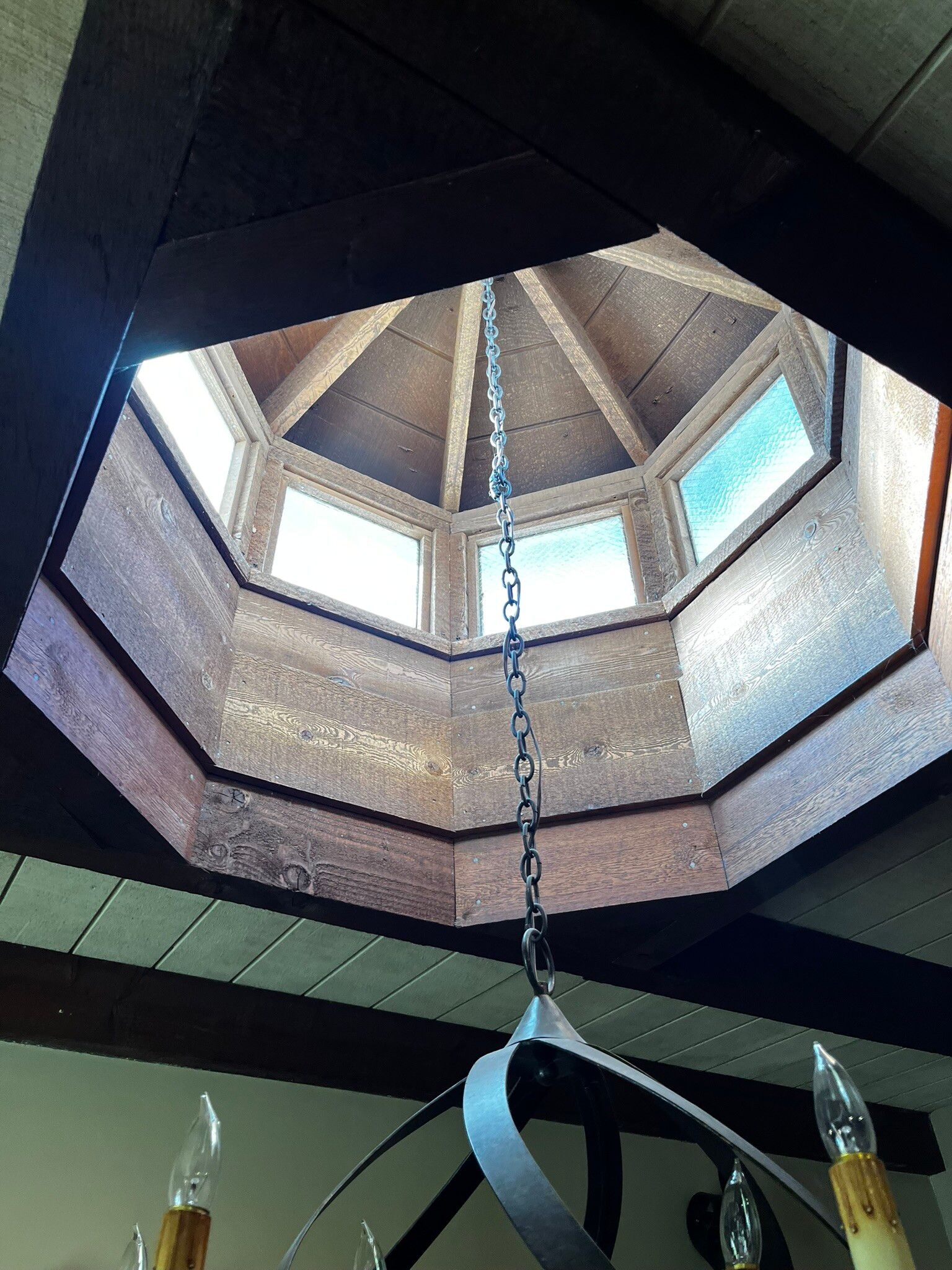 View up through an octagonal skylight with stone walls and a hanging chain chandelier.