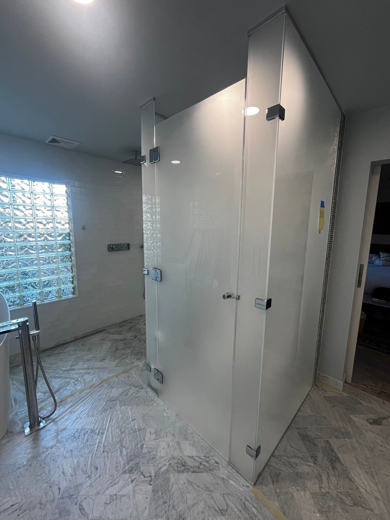 Modern restroom with white stall doors, gray tile floor, and a textured glass window.