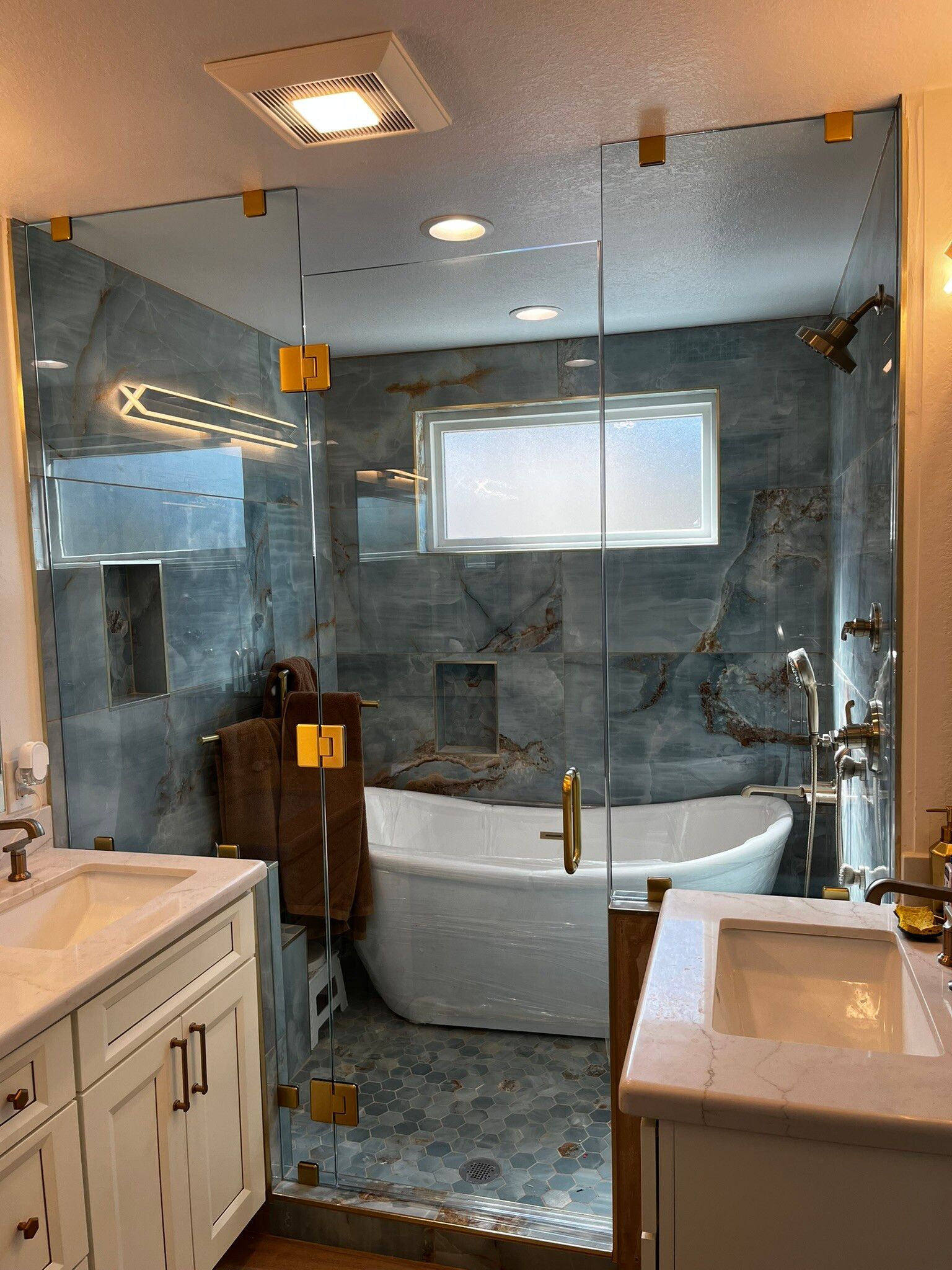 Modern bathroom with glass walk-in shower, white vanity, and freestanding tub against blue-gray tile.
