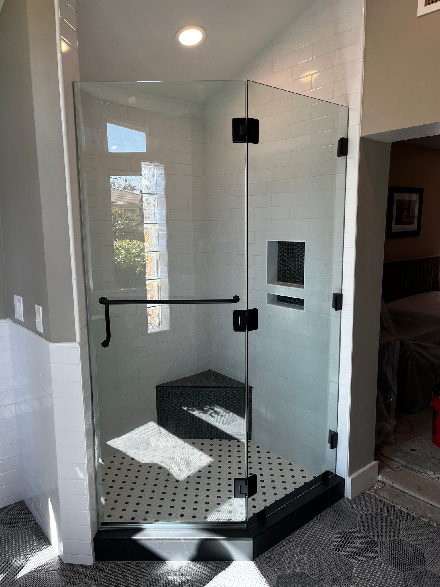 Glass shower enclosure with black trim, built-in bench, and white tile walls in a bathroom