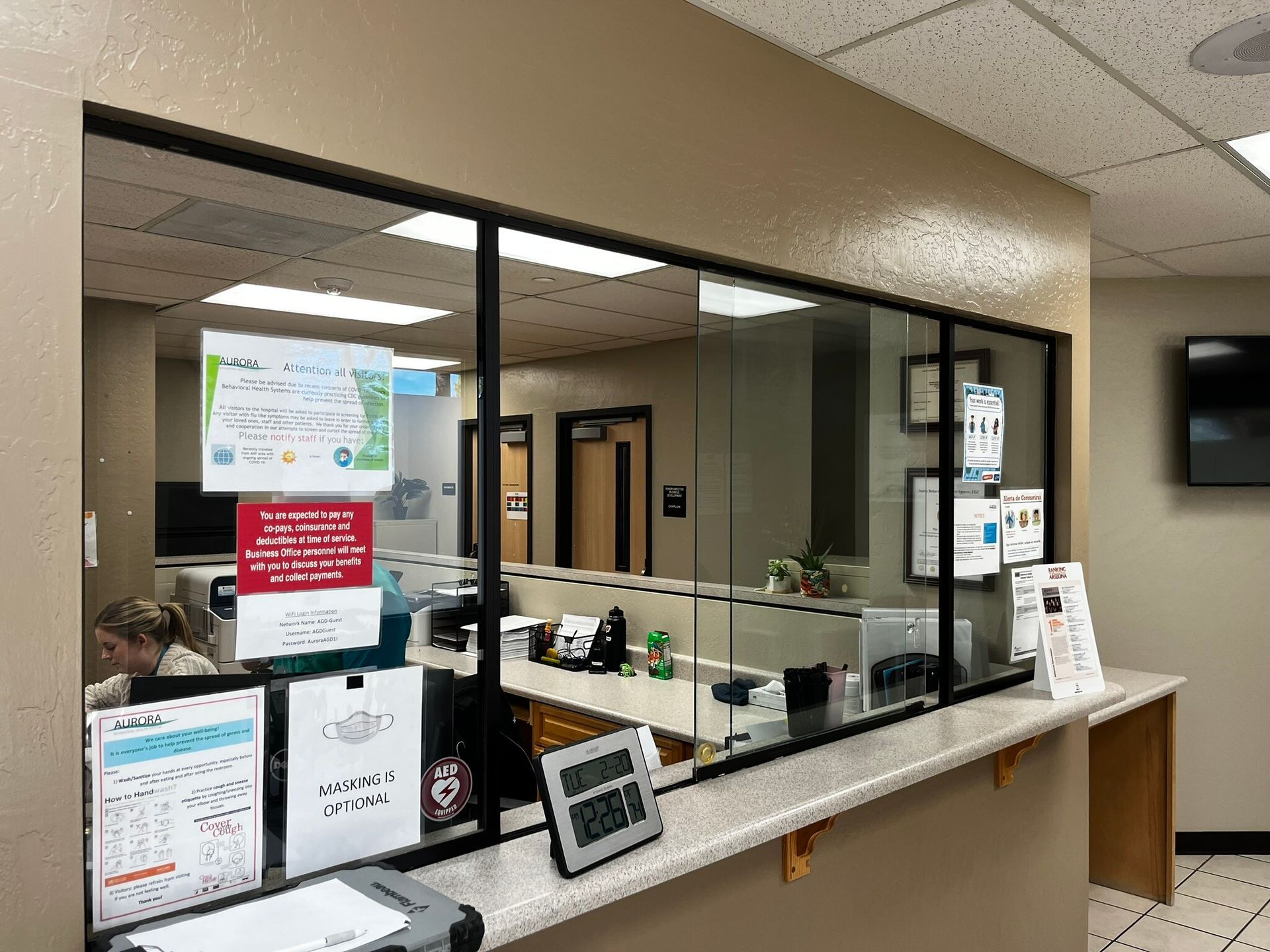 Bank lobby service counter behind glass with signs, brochures, and a payment terminal