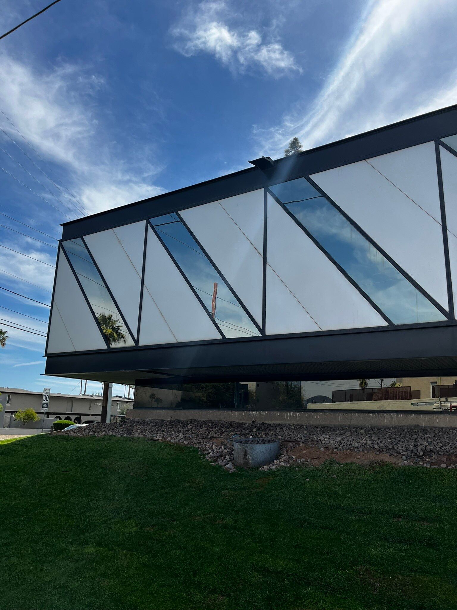 Modern angular glass building with reflective panels under a blue sky, viewed from a grassy foreground