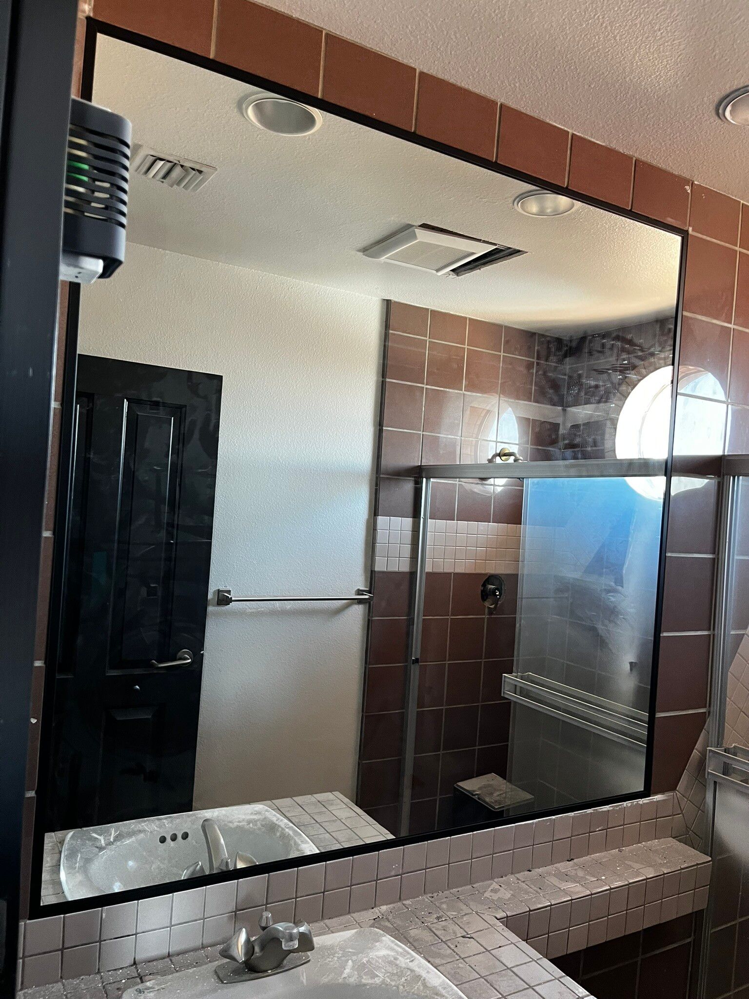 Bathroom vanity mirror reflecting a tiled shower and towel bars, with a sink and countertop below.