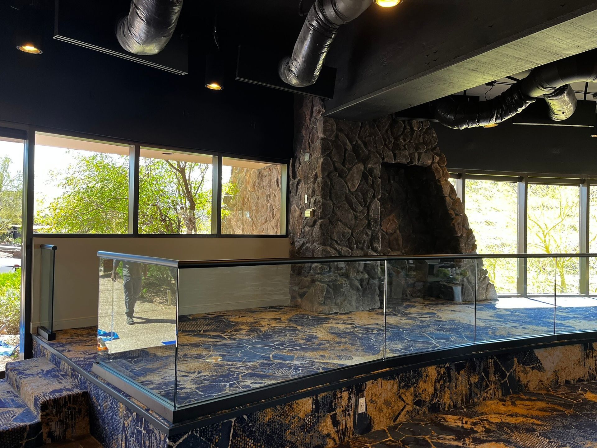 Empty modern interior with black ceiling, large windows, stone wall, and glossy blue reception counter