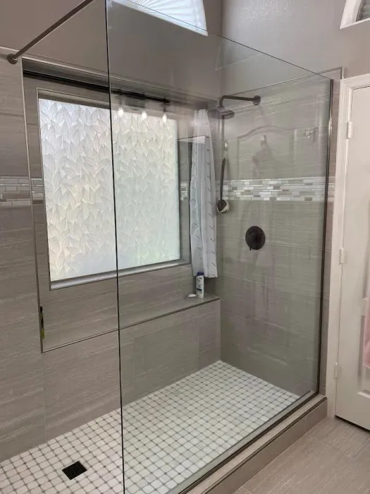 Modern walk-in shower with clear glass walls, white tile floor, and frosted window.