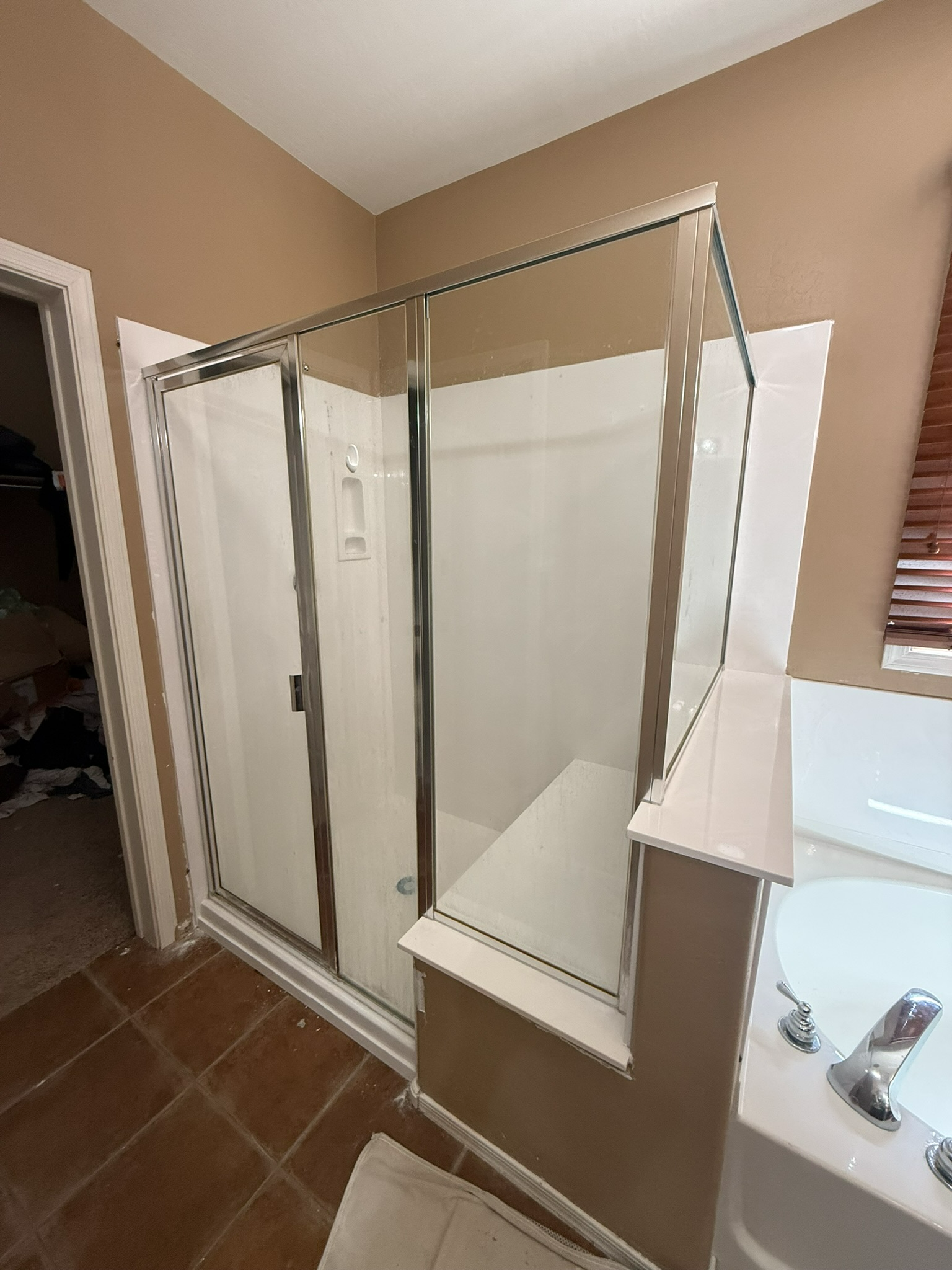 Bathroom with glass shower enclosure, beige walls, brown tile floor, and white sink counter.