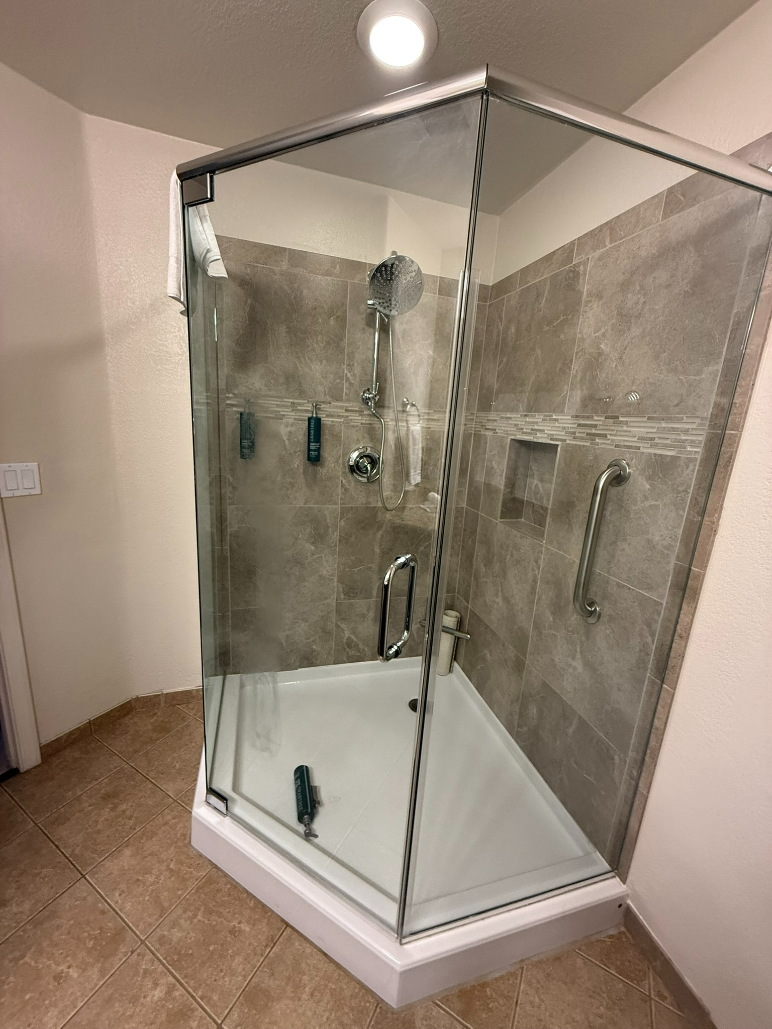 Corner glass shower enclosure with gray tile walls and white base in a bathroom