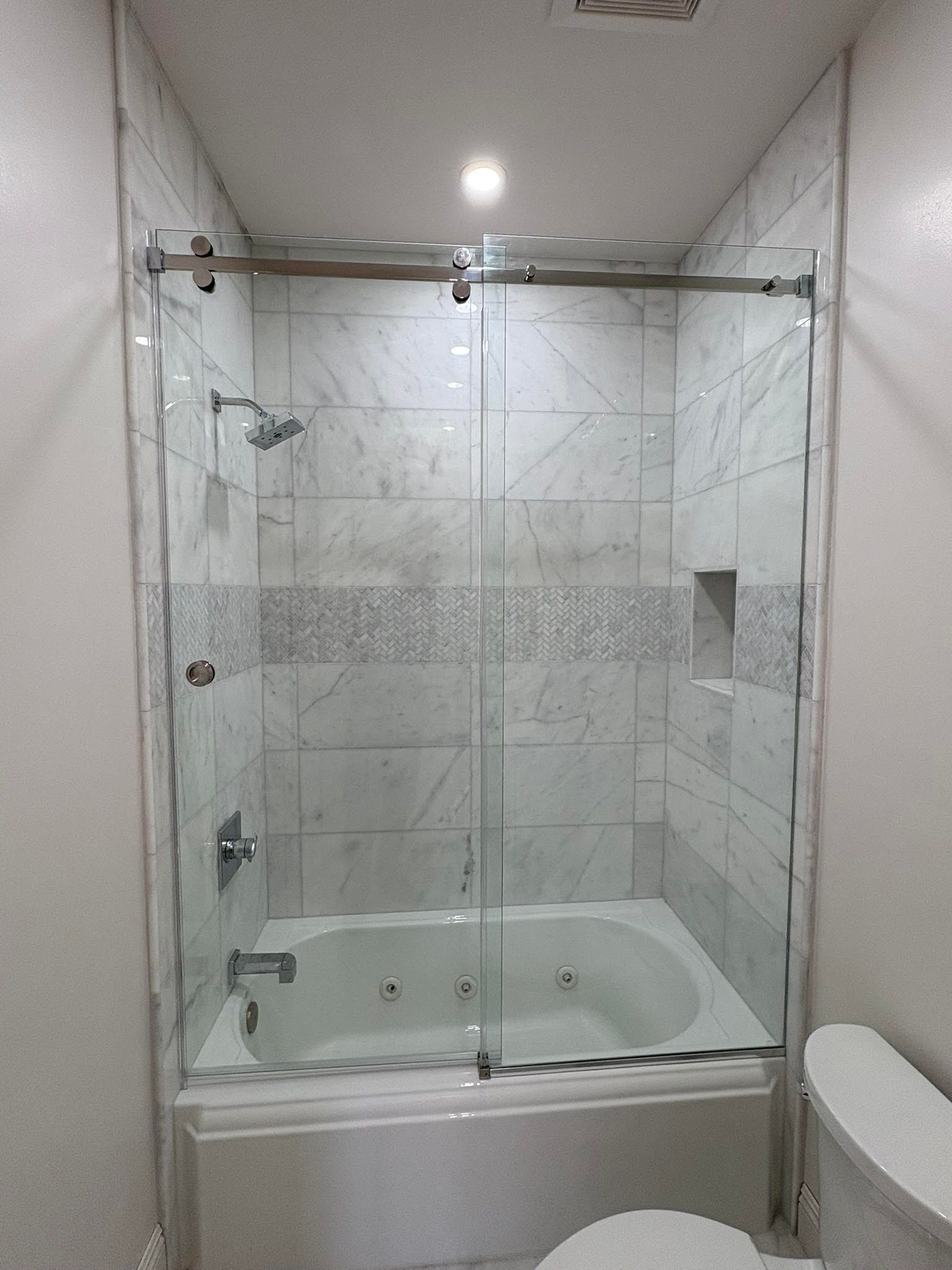 Glass-enclosed white tiled shower with built-in tub, chrome fixtures, and a ceiling light