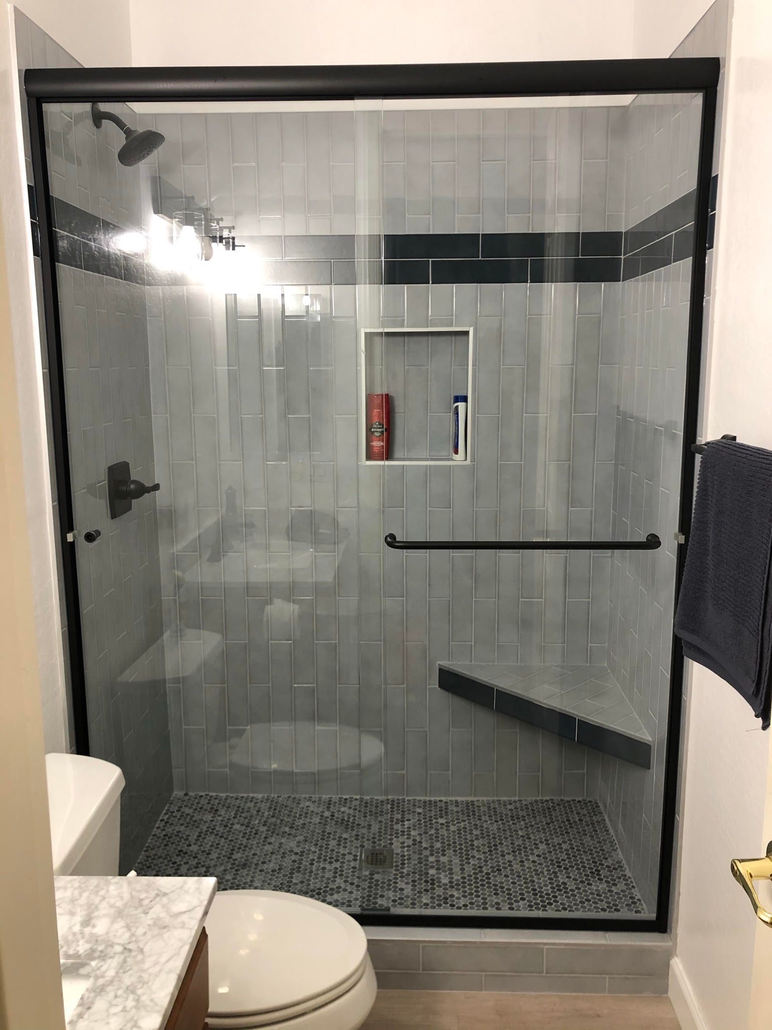 Glass walk-in shower with gray tile, bench, and pebble shower floor in a bathroom