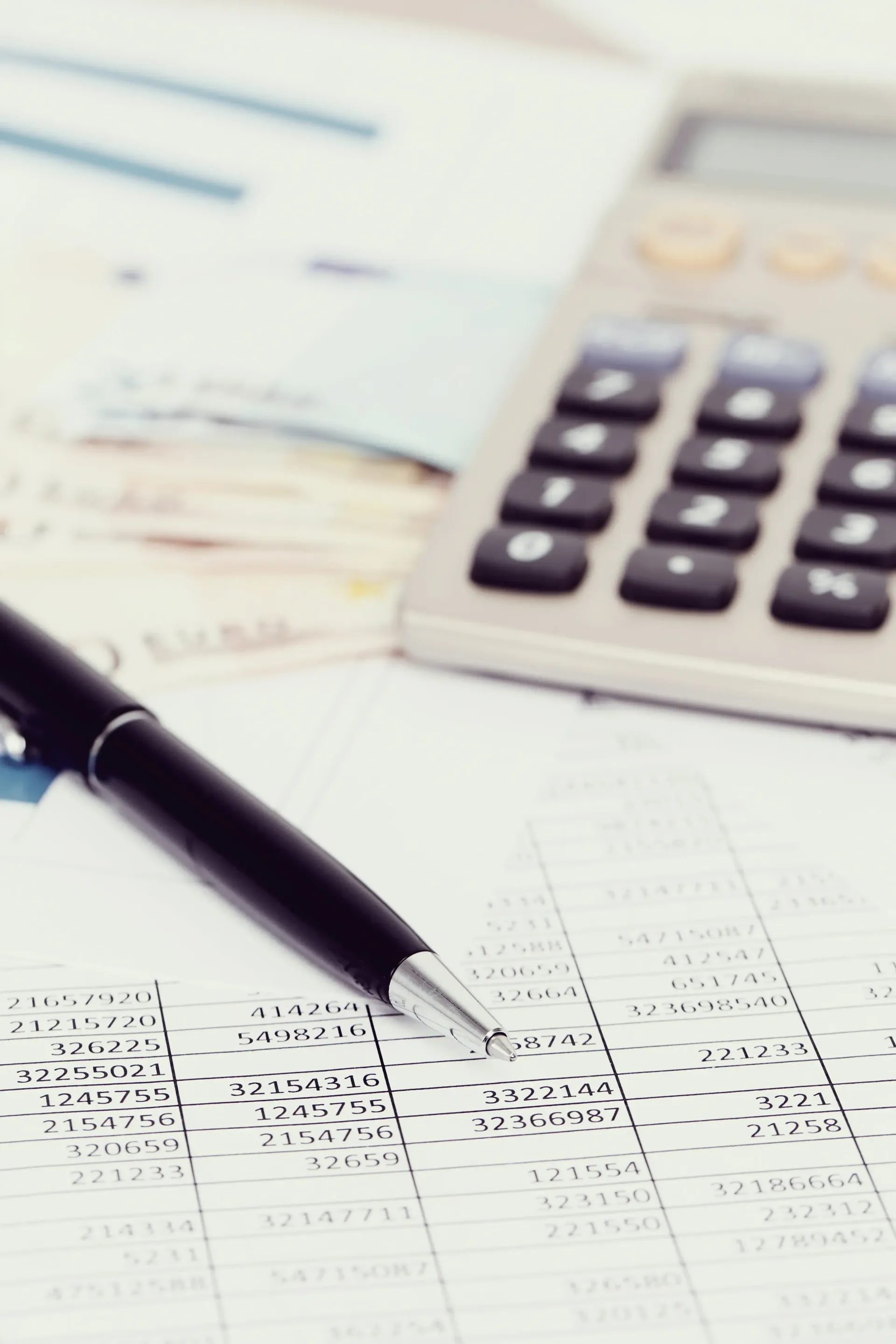 A black pen rests on a document with handwritten data, positioned next to a calculator and a stack of paper currency.