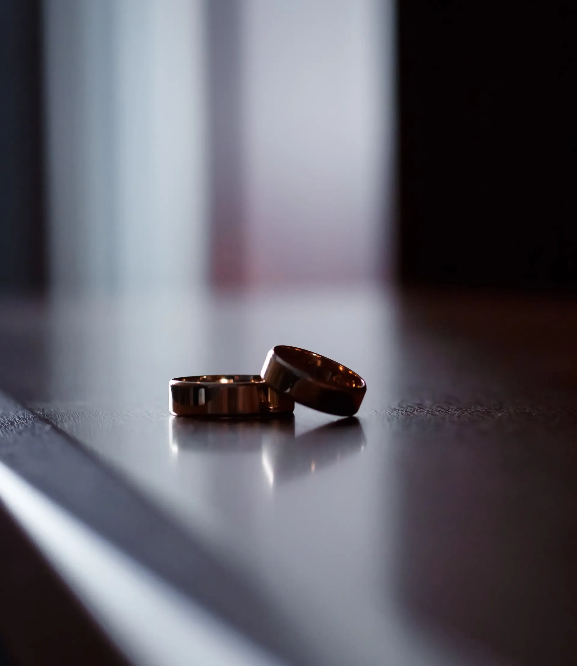 Two gold wedding bands resting on a smooth surface, captured in soft, dramatic lighting.