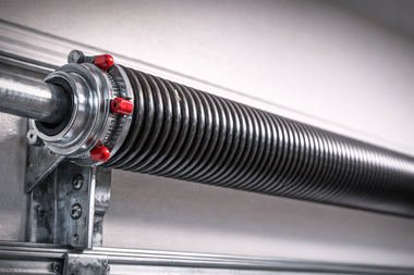 Garage door torsion spring, coiled black metal with red winding cones, attached to a metal bar and bracket.